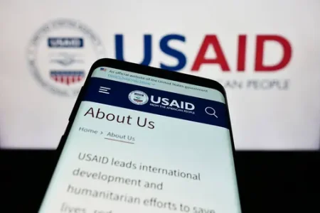 Smartphone with website of United States Agency for International Development (USAID) in front of logo. Focus on top-left of phone display.